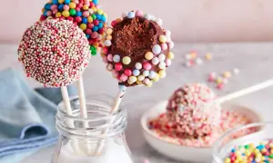 Bunte cake pops, verziert mit Zuckerstreuseln, warten darauf, vernascht zu werden. Einer ist angeknabbert und zeigt den schokoladigen Kern.