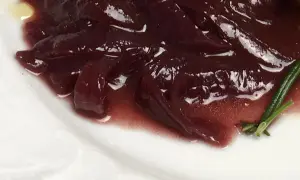 Portwein zwiebeln in einer glänzenden, dunklen Sauce auf einem weißen Teller, garniert mit Rosmarin.