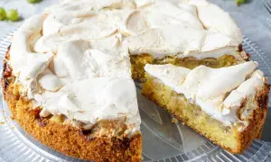 Omas stachelbeerkuchen mit luftiger Baiserhaube auf einem Tortenteller. Ein Stück ist bereits angeschnitten.