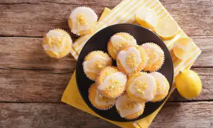 Zitronen-Muffins, frisch aus dem Thermomix, mit Zuckerguss und Zitronenschale bestreut, auf einem Holztisch.