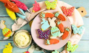 Bunte Osterkekse in Hasen-, Karotten- und Schmetterlingsformen, bereit für ein einfaches Osterkekse Rezept. Spritzbeutel mit Zuckerguss liegen bereit.