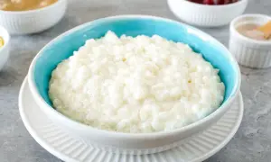 Cremiger Milchreis im blauen Schälchen, bereit für das perfekte Milchreis Rezept. Dazu Apfelmus und Kirschen.