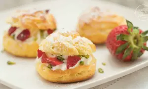 Saftige Windbeutel gefüllt mit Sahne, Erdbeeren und Pistazien, bestäubt mit Puderzucker. Ein köstliches Dessert.