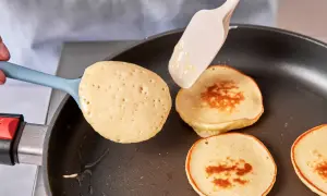 Pancakes rezept mit joghurt: goldbraune Pfannkuchen werden in einer Pfanne gebacken, ein Löffel Teig wird hinzugefügt.