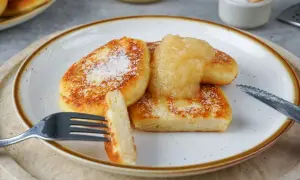 Goldbraune Quarkkeulchen, bestreut mit Puderzucker, serviert mit Apfelmus. Ein köstliches Quarkkeulchen Rezept zum Genießen.
