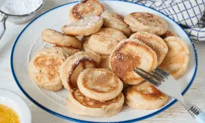 Ein Teller voller goldbrauner Poffertjes, bestäubt mit Puderzucker. Ein Gabel liegt bereit, um das leckere Poffertjes Rezept zu genießen.