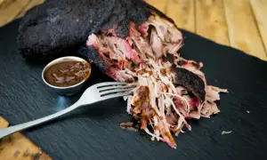 Saftiges Pulled Pork, perfekt für ein gerupftes Rezept. Eine Gabel nimmt zarte Fleischfasern auf, daneben eine Schale BBQ-Sauce.