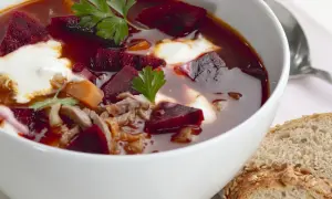 Herzhaftes Borschtsch-Rezept: Rote Bete, Fleisch und ein Klecks Sahne in einer Schüssel, dazu Brot.