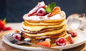Ein Stapel amerikanischer Pancakes, bestäubt mit Puderzucker und garniert mit frischen Beeren und Minze.