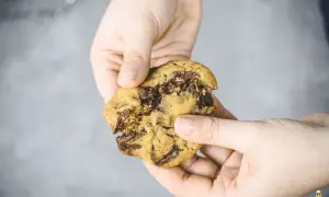 Hände halten einen zerbrochenen schoko cookie mit geschmolzener Schokolade.