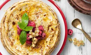 Gestapelte Pfannkuchen ohne Mehl, beträufelt mit Honig und garniert mit frischen Beeren und Minze. Ein köstlicher Genuss!