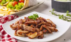 Saftiges Fleisch für ein köstliches Gyros Rezept, garniert mit Petersilie. Daneben liegen Gyros-Wraps und ein Gurkensalat.