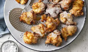 Goldbraune Apfelkrapfen, frisch aus der Pfanne, mit Puderzucker bestäubt, liegen auf einem Sieb.