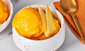 Erfrischendes Mango-Sorbet in einer Schale, garniert mit Mangostücken. Daneben liegt ein goldener Löffel auf einem orangen Tuch.