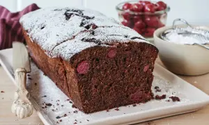 Saftiger schoko kirsch kuchen, bestäubt mit Puderzucker. Daneben eine Schale mit Kirschen und ein Sieb.