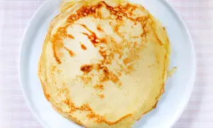 Ein Stapel goldbrauner, veganer Pfannkuchen liegt auf einem weißen Teller. Perfekt für ein leichtes Frühstück.