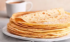 Ein Stapel goldbrauner Pfannkuchen, bestäubt mit Puderzucker, wartet auf ein leckeres Pfannkuchen Rezept. Daneben eine Tasse Kaffee.
