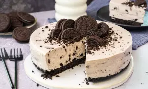 Ein köstlicher Oreo Kuchen, dekoriert mit ganzen und zerbrochenen Keksen, wartet darauf, angeschnitten zu werden. Daneben liegen Gabeln und ein Glas Milch.