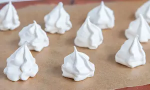 Weiße Baiser-Häufchen, bereit für das Baiser Rezept. Sie liegen auf Backpapier und sehen luftig und leicht aus.