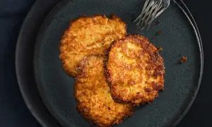 Drei goldbraune Kartoffelpuffer liegen auf einem dunklen Teller. Perfekt für den Thermomix!