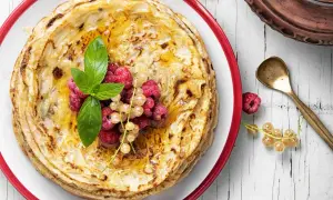 Ein Stapel goldbrauner Pfannkuchen, garniert mit Beeren und Minze. Der Pfannkuchenteig ist perfekt gebacken und mit Honig beträufelt.