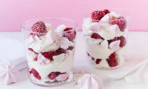 Zwei Gläser mit Himbeer Baiser Dessert, geschichtet mit Sahne, frischen Himbeeren und Baiserstückchen.