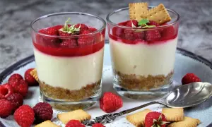 Zwei Gläser mit cremigen Desserts, garniert mit Himbeeren und Keksen. Perfekt für Ihre nächsten Dessert Rezepte.