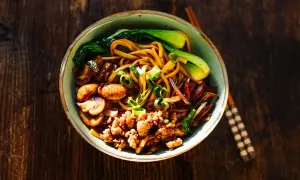 Herzhafte Udon Nudeln mit gebratenem Tofu, Pilzen, Pak Choi und Frühlingszwiebeln auf einem rustikalen Holztisch.