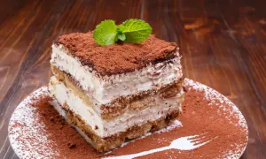 Ein Stück cremiges Tiramisu ohne Ei, bestäubt mit Kakao und garniert mit Minze, auf einem Teller mit Kakaopulver-Gabelabdruck.
