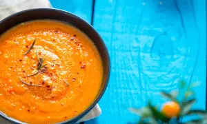 Eine cremige Tomatensuppe, zubereitet im Thermomix, garniert mit Rosmarin und Chiliflocken, serviert auf einem blauen Holztisch.