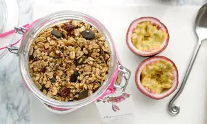 Glas mit selbstgemachtem Granola, Kürbiskernen und Trockenfrüchten. Daneben zwei Passionsfrüchte und ein Löffel.