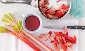Frischer Rhabarber wird geschnitten und mit Zucker für Rhabarberkompott vorbereitet. Ein Messer und eine Schüssel mit rotem Saft liegen bereit.