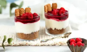 Zwei Gläser mit einem köstlichen, warmer nachtisch: Kekskrümel, cremige Schicht, Himbeersoße und frische Beeren.
