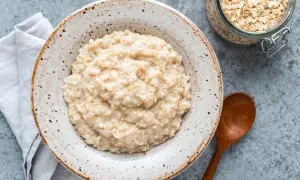 Cremiger Haferbrei in einer Schale, daneben ein Glas Haferflocken. Ein einfaches Porridge Rezept für einen gesunden Start.