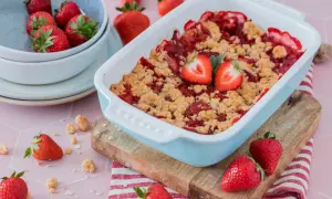 Erdbeer-Crumble im Auflaufform, garniert mit frischen Erdbeeren, daneben eine Schüssel mit Erdbeeren.