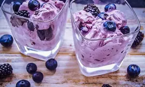 Zwei Gläser mit cremigem, lila gefärbtem frozen joghurt, garniert mit frischen Blaubeeren und Brombeeren.