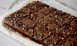Saftige Zucchini-Brownies, bestreut mit Schokoladenstückchen, auf Backpapier.