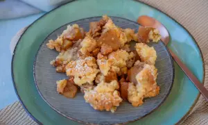 Ein Teller mit köstlichem Apfel-Crumble, bestäubt mit Puderzucker. Die warmen Apfelstücke und die knusprige Streuselhaube laden zum Genießen ein.