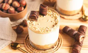 Ein Glas mit cremiger Kinder Bueno Creme, garniert mit Nüssen und Schokostückchen. Daneben liegen ganze Kinder Bueno Riegel.