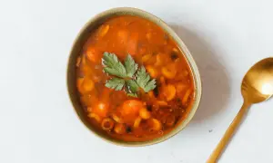 Herzhaftes Soljanka Rezept: Eine Schüssel voller würziger Suppe mit Oliven, Kapern und Kräutern, daneben ein goldener Löffel.
