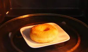 Ein einzelner Donut auf einem weißen Teller in einem Mikrowellenofen. So bleiben Donuts frisch.