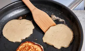 Buttermilch pancakes bräunen in der Pfanne, eine Holzspachtel wendet sie.