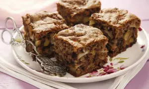 Vier Stücke saftiger Apfel Walnuss Kuchen auf einem Teller mit floralem Muster, daneben eine antike Kuchenzange.