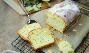 Saftiger Zucchini Kuchen mit Zuckerguss, frisch angeschnitten auf einem Gitter. Daneben liegen geriebene Zucchini und ein Hobel.