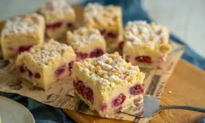 Saftiger Kirschkuchen mit Pudding und Streuseln, bestäubt mit Puderzucker. Ein Stück wird gerade serviert.