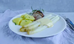 Weißer Spargel mit Sauce Hollandaise, Kartoffeln und Fleisch auf einem Teller.