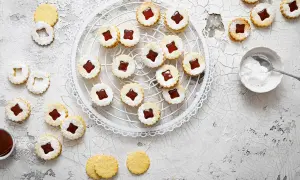 Spitzbuben mit Mandeln und Marmelade, bestäubt mit Puderzucker, auf einem Gitter und Tisch verteilt.