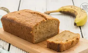 Saftiges Bananenbrot mit Dinkelmehl, frisch gebacken und auf einem Holzbrett angerichtet. Eine Scheibe ist bereits abgeschnitten.