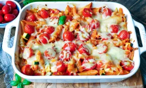 Ein köstlicher nudelauflauf vegetarisch mit Penne, Kirschtomaten und geschmolzenem Käse in einer weißen Auflaufform.
