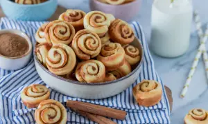 Mini Zimtschnecken in einer Schüssel, daneben Zimtstangen und ein Glas Milch.